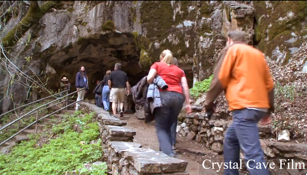 A group of people approaches the entrance to a cave along a path lined with rock walls