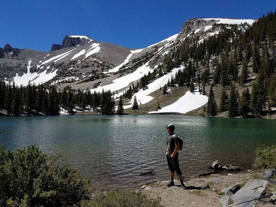 A visitor stands in front of Stella Lake looking at the Wheeler Peak ridgeline, which is dappled in snow