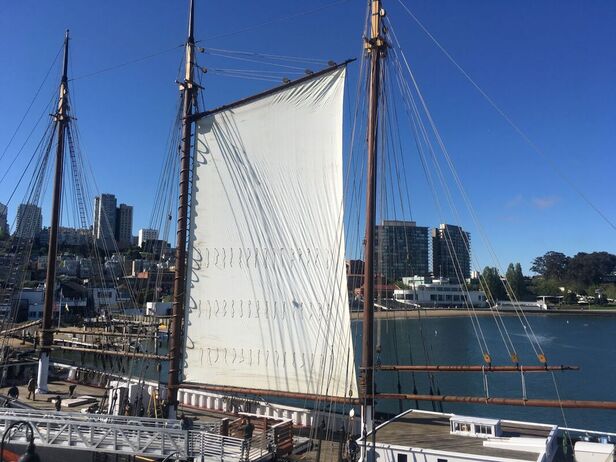The new gaff sail rigged on the C.A. Thayer in harbor with buildings of San Francisco in the background
