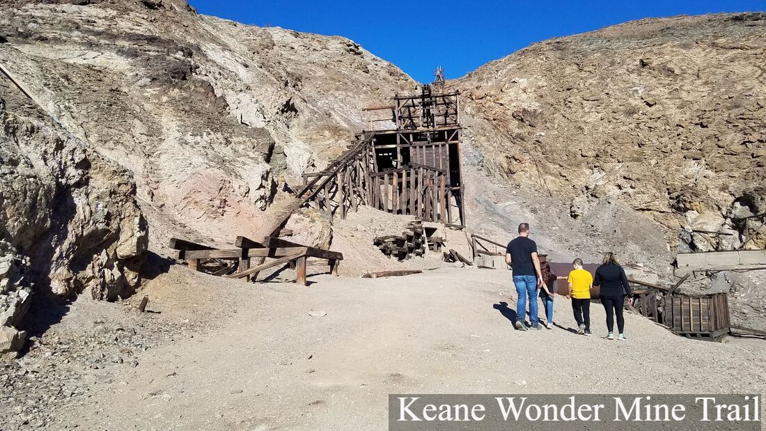 A group of four people walks toward old wooden mining structures at Keane Wonder Mine