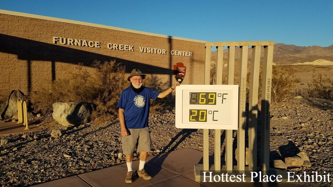A person with a beard stands in front of the thermometer exhibit in front of Furnace Creek Visitor Center