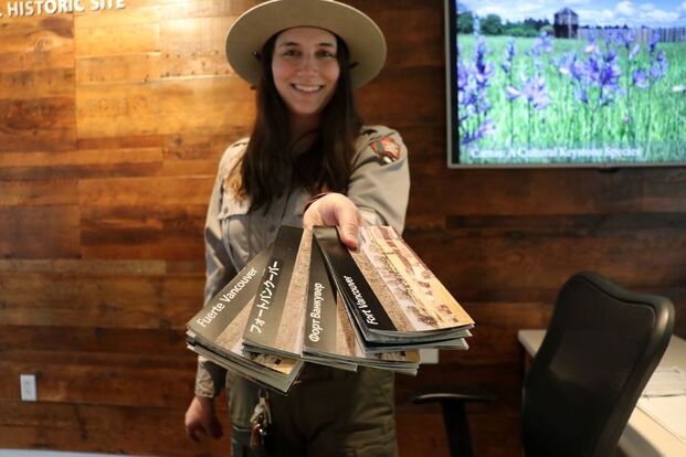 A ranger stands holding four brochures out to the camera, each in a different language
