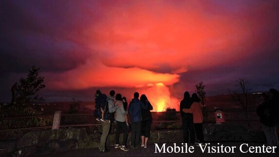 A group of visitors watches red spewing lava in the distance; the words 