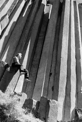 A black and white photo of an individual sitting on top of the one of the basalt columns of Devils Postpile