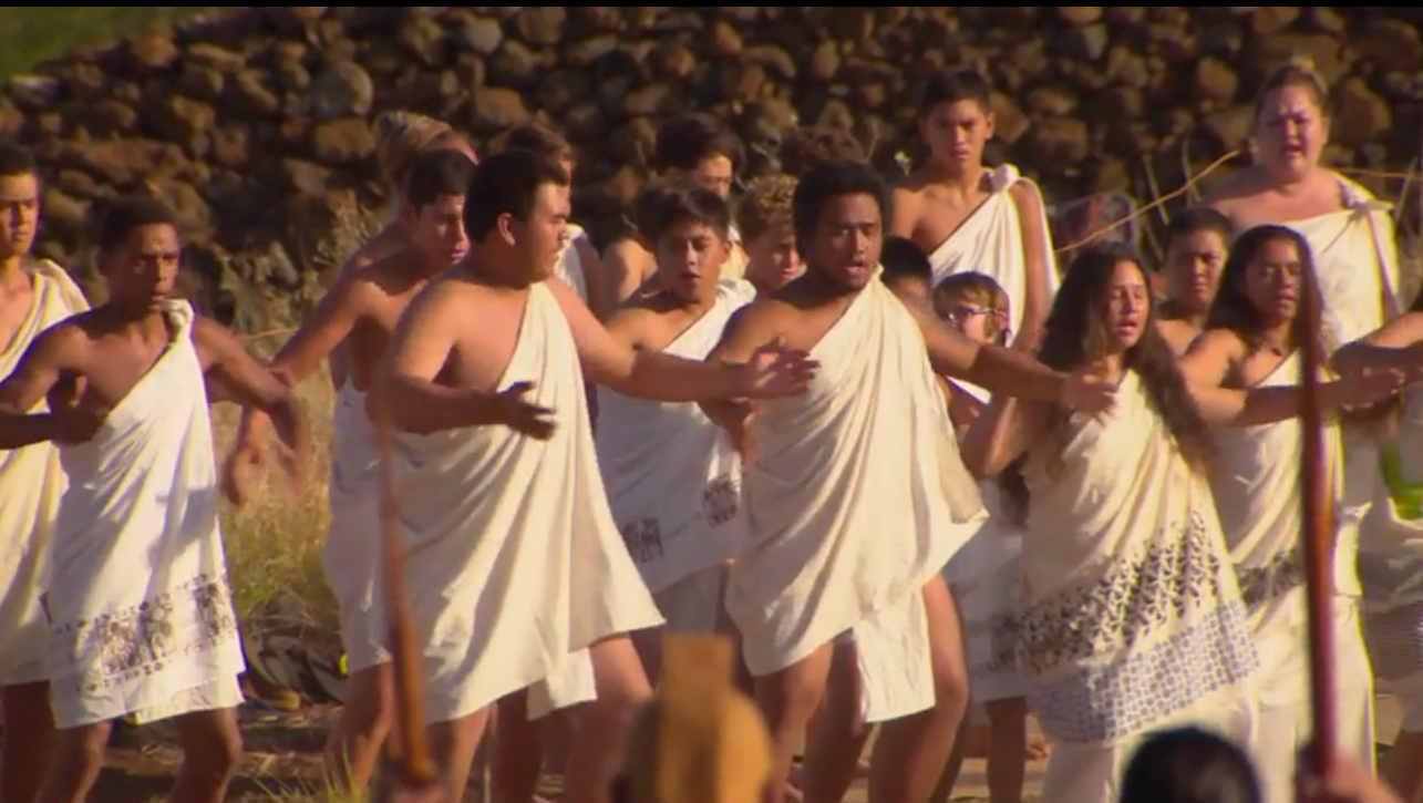 A group of people dressed in traditional white garments stands with arms open performing a dance