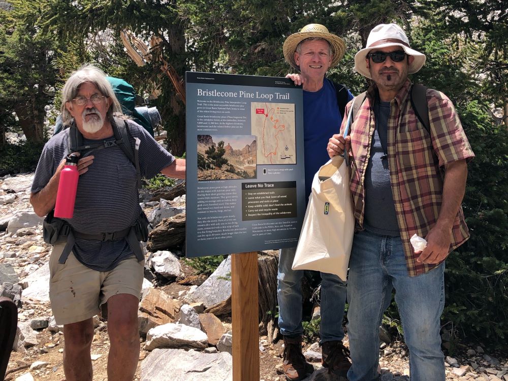 Three people stand next to a trailhead sign that says "Bristlecone Pine Loop Trail"