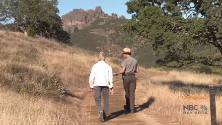 A ranger and another person walk and talk on a trail while walking toward the Pinnacles rock formation 