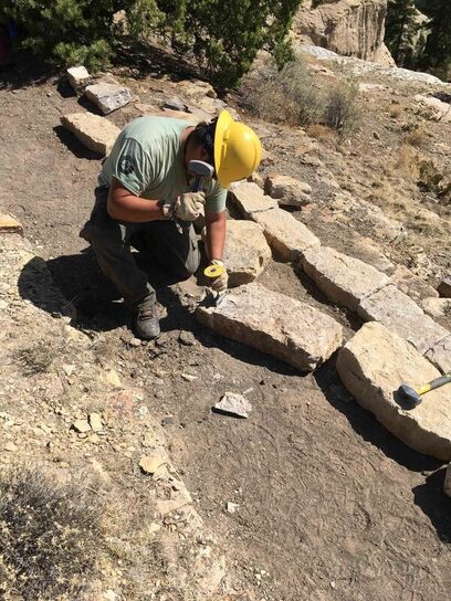 An Ancestral Lands Conservation Corps crew member trims stone borders