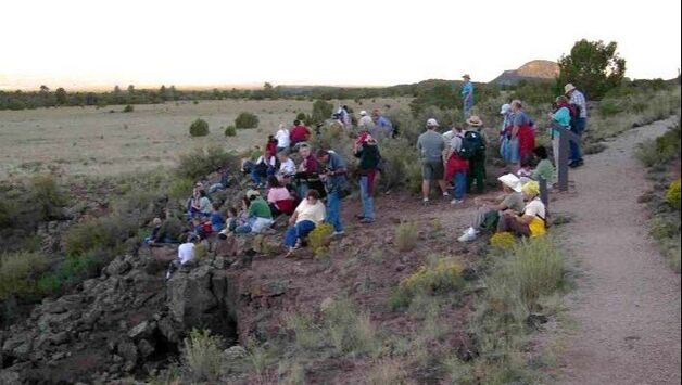 A group of people stand and sit among lava rocks looking out over a chasm