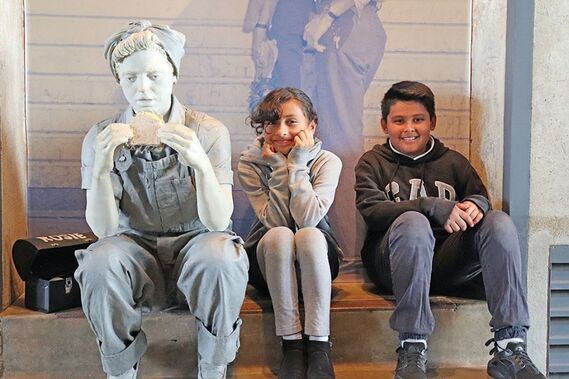 Two children sit next to a life-size statue 