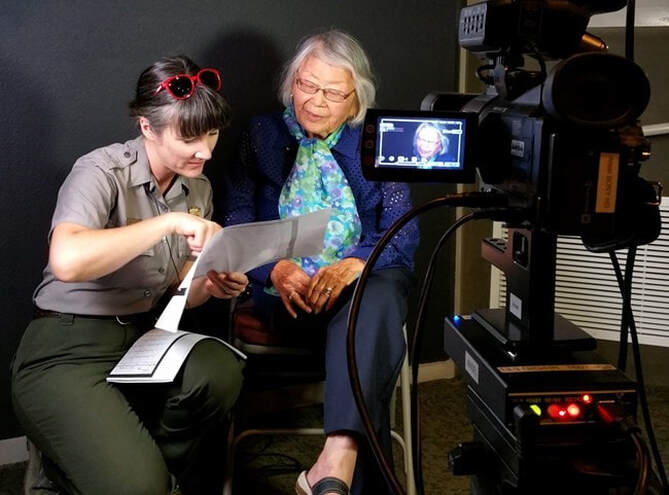 A ranger looks over a document with a former Manzanar incarceree in front of a camera