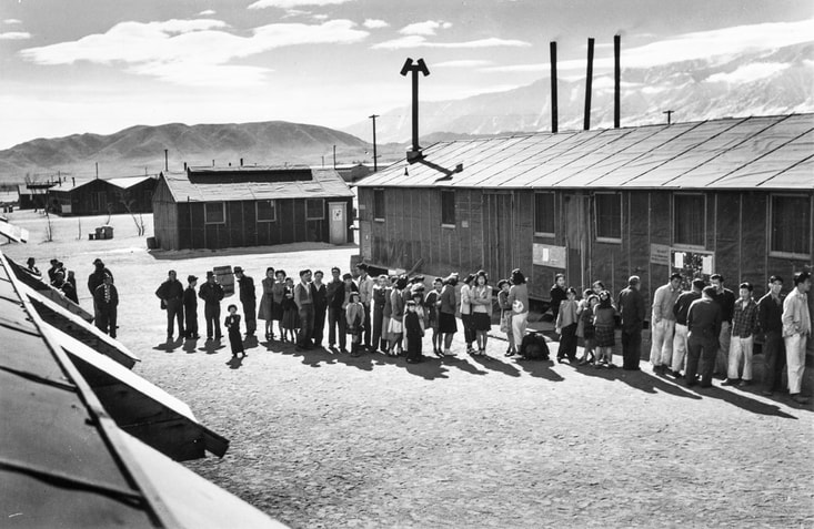 Historic Ansel Adams photo of incarcerees waiting in line outside a building at Manzanar