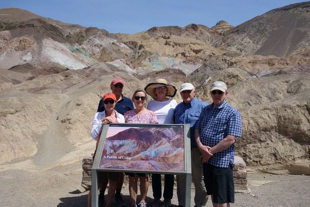People stand behind a new wayside educational sign with the Artists Pallette geological feature in the background