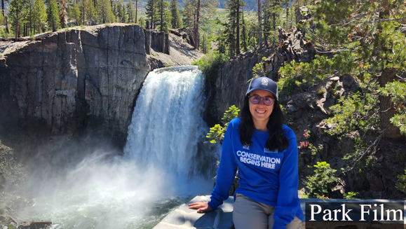 A person faces the camera, smiling, with Rainbow Falls in the background