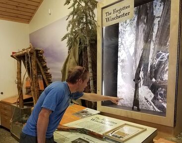 A visitor points at a rifle inside the Great Basin visitor center exhibit labeled 