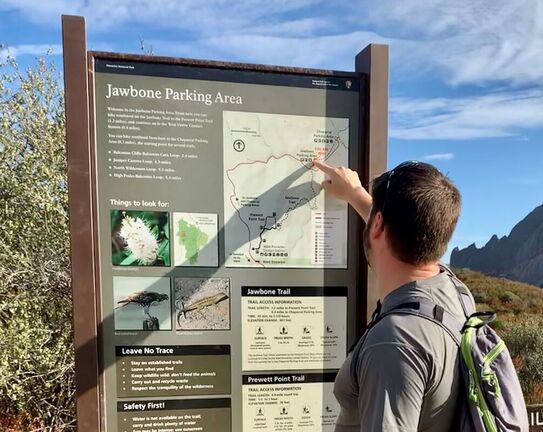 A visitor locates themself on the map of a trailhead sign