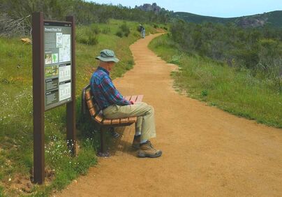 A visitor sits on a bench next to a trail sign along the Prewett Point universal access path