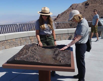 A National Park Service ranger and a visitor touch a bronze relief model of Badwater Basin in Death Valley