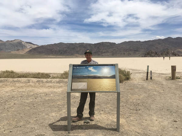 A ranger stands behind a new wayside educational sign with the vast expanse of the Racetrack Playa behind