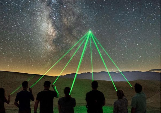 7 people point laser pointers at a single star in the dark night sky of Death Valley