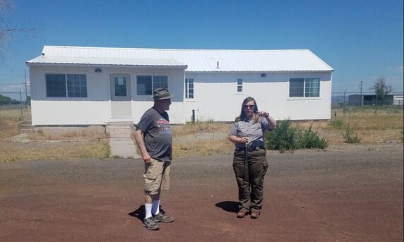 A visitor listens to a ranger in front of a white building, the future Tule Lake Visitor Center