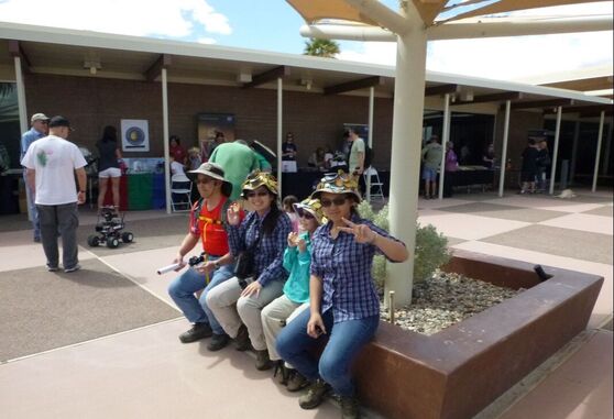 A group of four people sits along the edges of a planter in a courtyard with other people milling about in the background