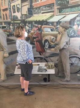 A visitor wearing a mask views an exhibit with a life-size statue of a teenager on standing with a bicycle