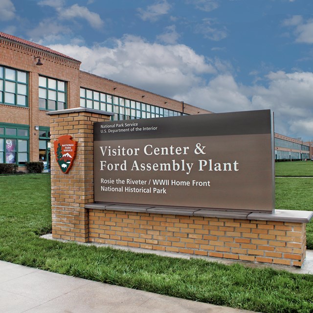 A large National Park Service sign that says, "Visitor Center & Ford Assembly Plant"