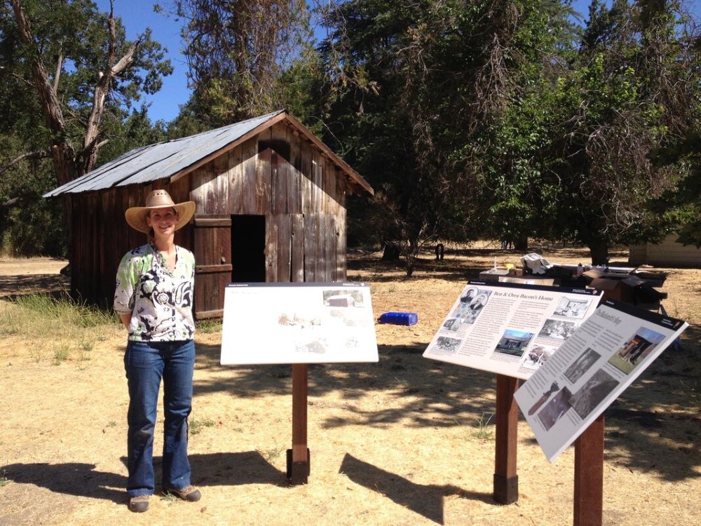 A person in a cowboy hat stands next to three educational signs with a wooden barn in the background