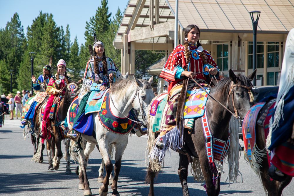 Several people ride horses, each adorned in traditional Nimiipuu textiles