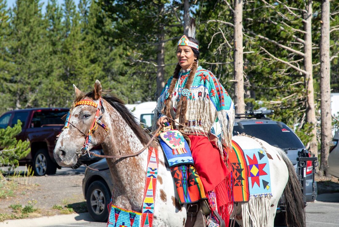 A Nez Perce person rides a horse adorned with colorful beadwork and textiles
