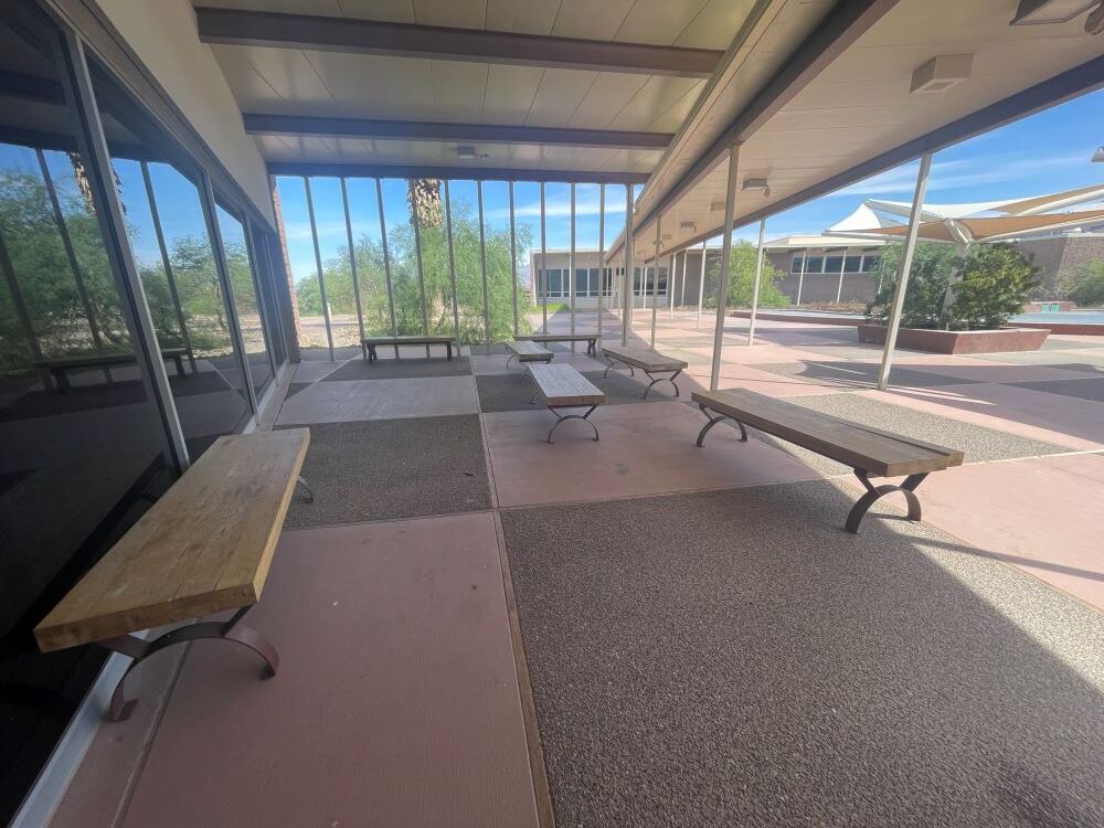 a group of wooden benches sits under a breezeway of a tiled courtyard