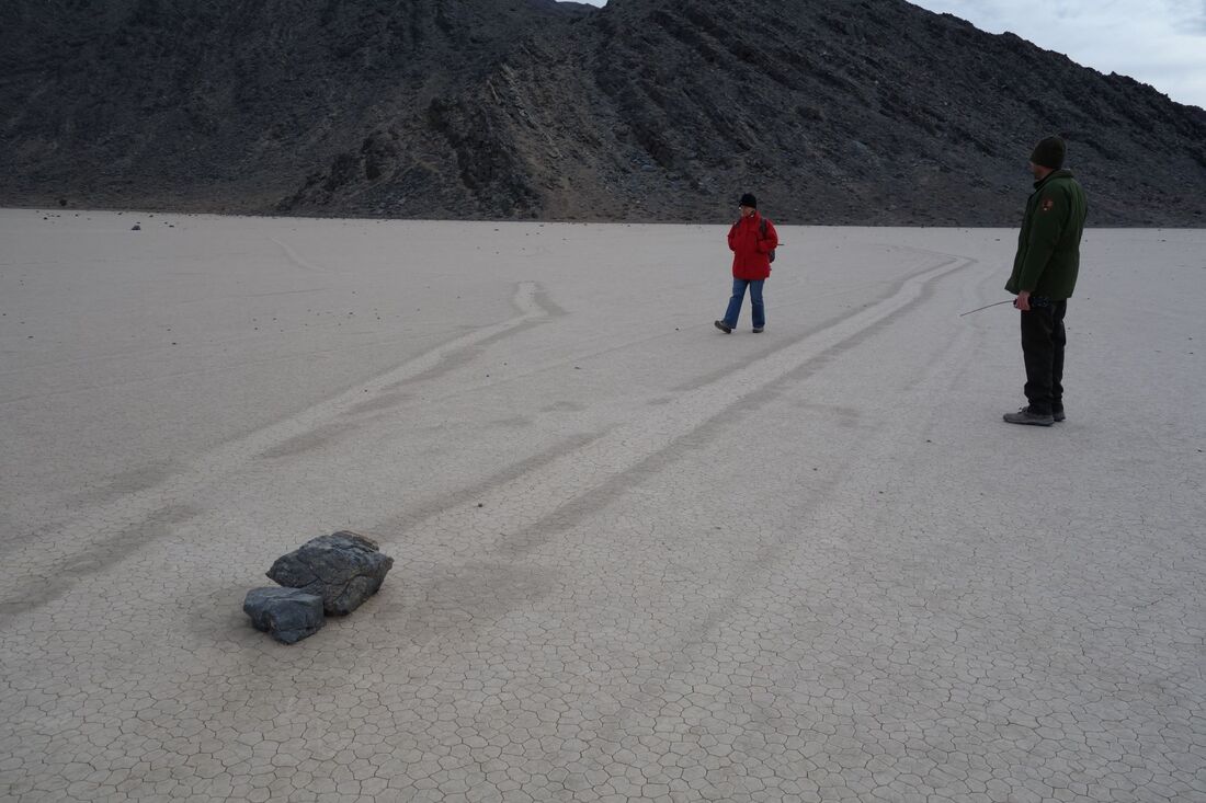 People standing near 2 moving rocks and their tracks