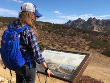 A person stands reading an educational sign with the Pinnacles rock formation in the background