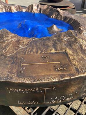 A close-up of the bronze sculpture, showing the scale, lake depth in English and braille