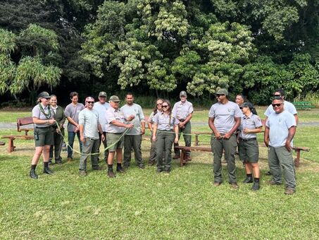 A group of NPS rangers stands around a green ribbon, ready to cut, with new wooden benches behind them