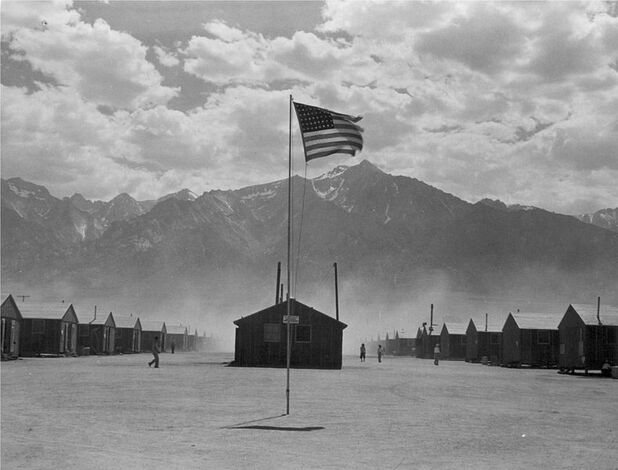 Historic photo of flag, barracks, and mountains at Manzanar