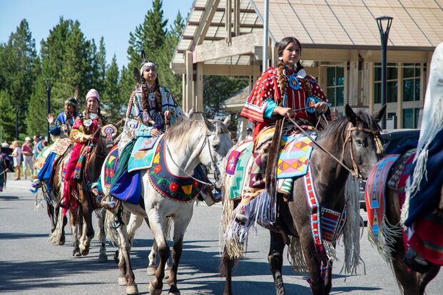 A group of Nez Perce people ride horses adorned with beaded items