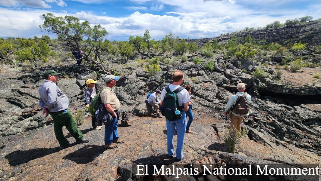 A group of people stands on a lava landscape looking down toward the opening to a lava tube cave