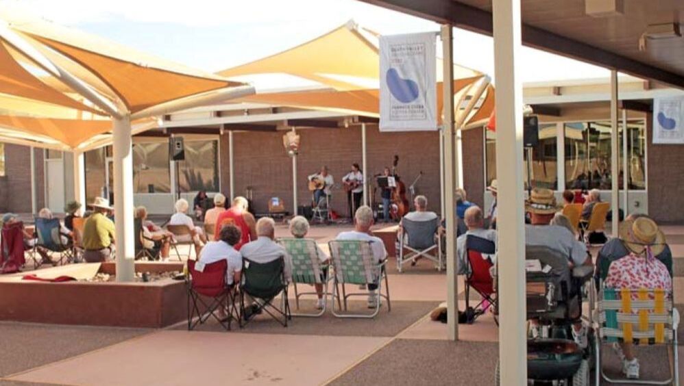 People sit in folding chairs watching the band, South Coast, play in the Furnace Creek Courtyard underneath triangular shade structures
