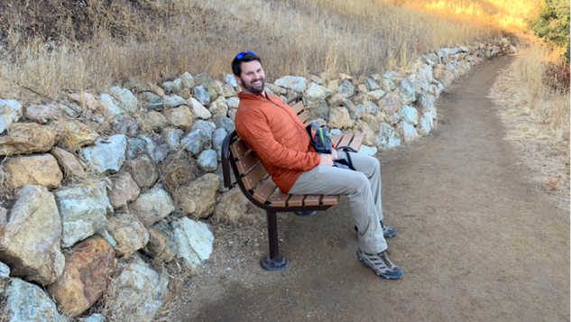A person sits on a bench aside a dirt trail and a rock wall