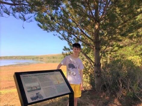 A visitor stands next to a wayside educational sign with Drakes Estero in the background