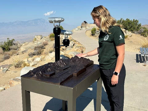 A visitor touches a relief map. Viewing scopes and the Coachella Valley and are in the background