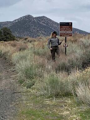 A National Park Service ranger stands adjacent to a new set of boundary signs with a large mountain looming in the background