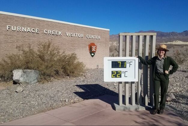 A National Park Service ranger stands in front of the thermometer exhibit and Furnace Creek Visitor Center