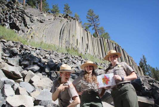 Three National Park Service rangers in uniform stand in front of the Devils Postpile basalt column formation