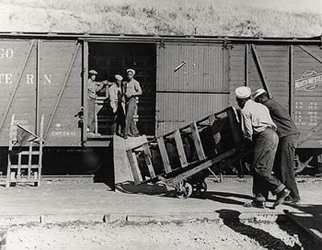 Black and white image of sailors loading crates onto railway cars