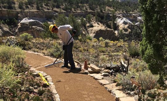 A trail crew member rakes a new dirt path with rock paver stones along edges