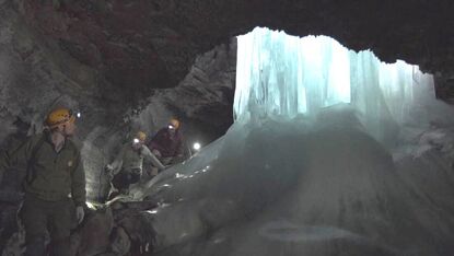 People wearing protective gear navigate a dark cave with a large ice formation