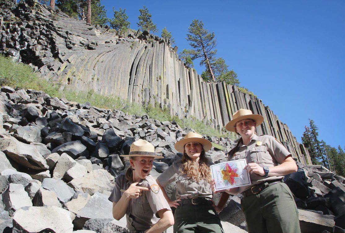 Three National Park Service rangers in uniform stand in front of the Devils Postpile columnar basalt formation